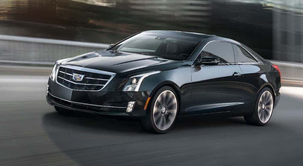 A black used Cadillac for sale, a 2019 Cadillac ATS, is driving on a blurry city street.