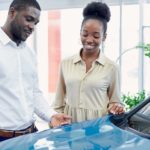 A couple is looking at a blue car inside a used car dealership showroom.