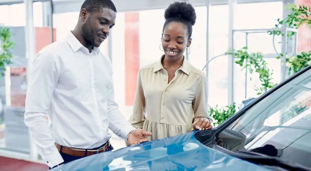 A couple is looking at a blue car inside a used car dealership showroom.