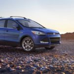 A blue 2013 used Ford Escape is parked on a rocky beach.