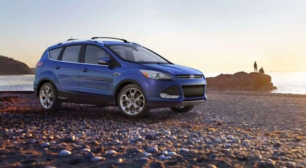 A blue 2013 used Ford Escape is parked on a rocky beach.