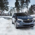 A dark blue 2020 Chevy Equinox is driving on a snowy road.