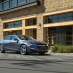 A gray 2020 Chevy Malibu is parked in front of a tan stone building.