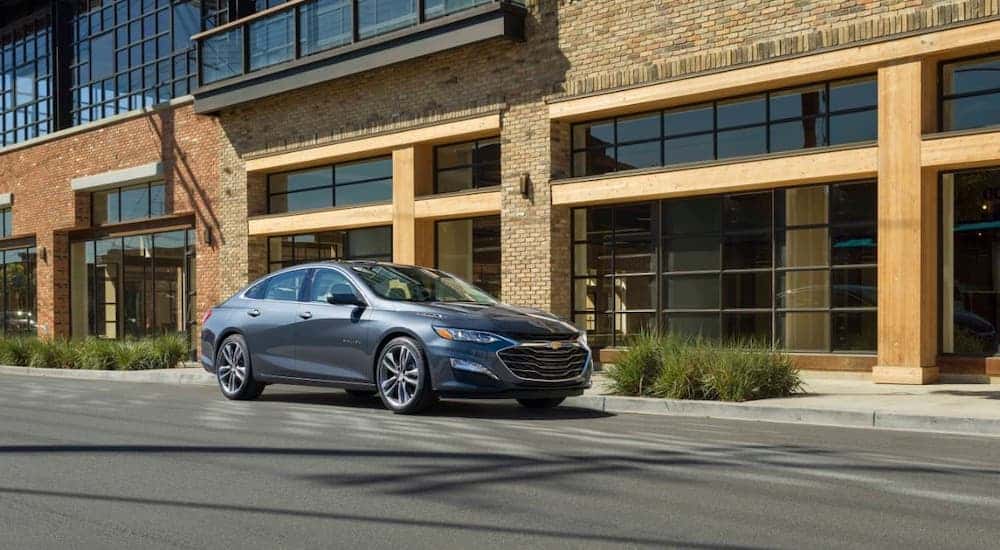 A gray 2020 Chevy Malibu is parked in front of a tan stone building.