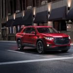 A red 2020 Chevy Traverse RS is parked at a stop light on a city street at night.