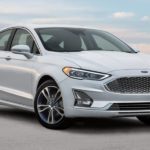 A white 2020 Ford Fusion is parked in front of a low cement wall and blue, cloudy sky after winning the 2020 Ford Fusion vs 2020 Mazda 6 comparison.