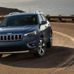 A grey 2020 Jeep Cherokee is driving around a corner past the ocean.