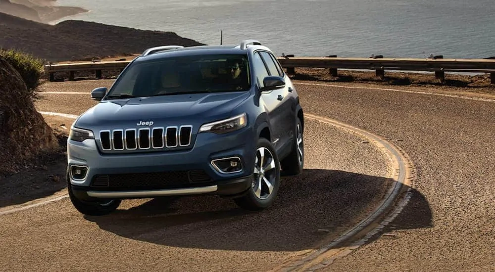A grey 2020 Jeep Cherokee is driving around a corner past the ocean.