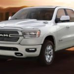 A white 2020 Ram 1500 is driving on a highway at sunset after winning the 2020 Ram 1500 vs 2020 Ford F-150 comparison.