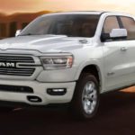 A white 2020 Ram 1500 is driving on a highway at sunset after winning the 2020 Ram 1500 vs 2020 Ford F-150 comparison.