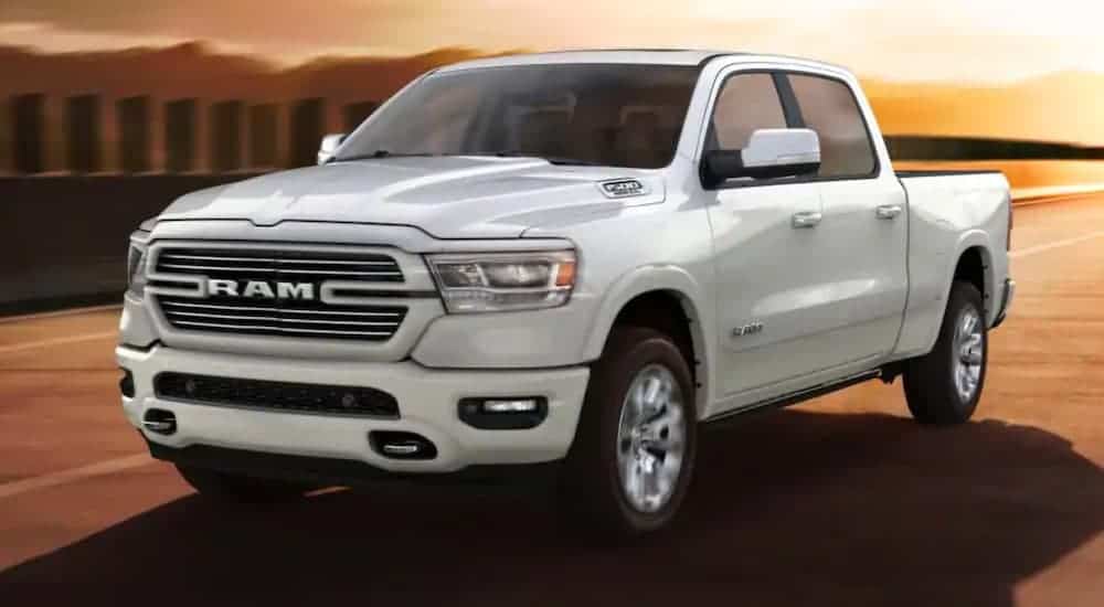 A white 2020 Ram 1500 is driving on a highway at sunset after winning the 2020 Ram 1500 vs 2020 Ford F-150 comparison.