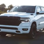 A white 2020 Ram 1500 is parked in an open lot with trees behind it.