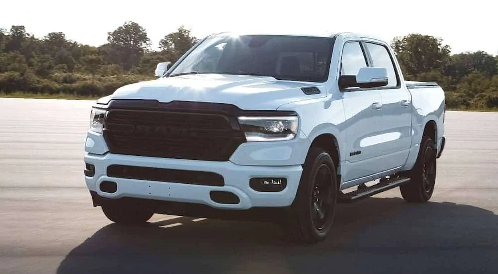 A white 2020 Ram 1500 is parked in an open lot with trees behind it.