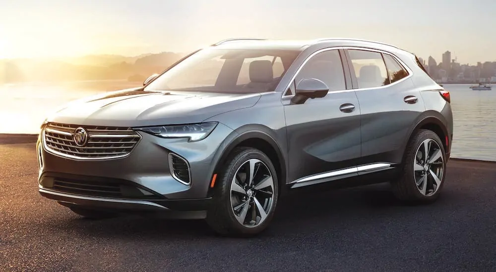 A silver 2021 Buick Envision is parked in front of a river and city at sunset.