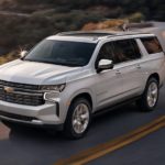 A silver 2021 Chevy Suburban is driving on a winding road along a mountainside.