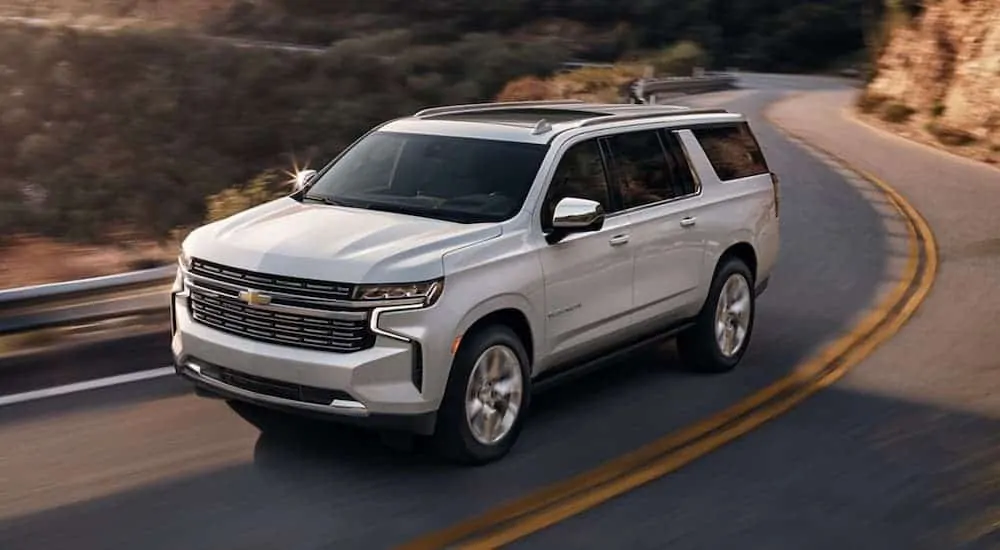 A silver 2021 Chevy Suburban is driving on a winding road along a mountainside.