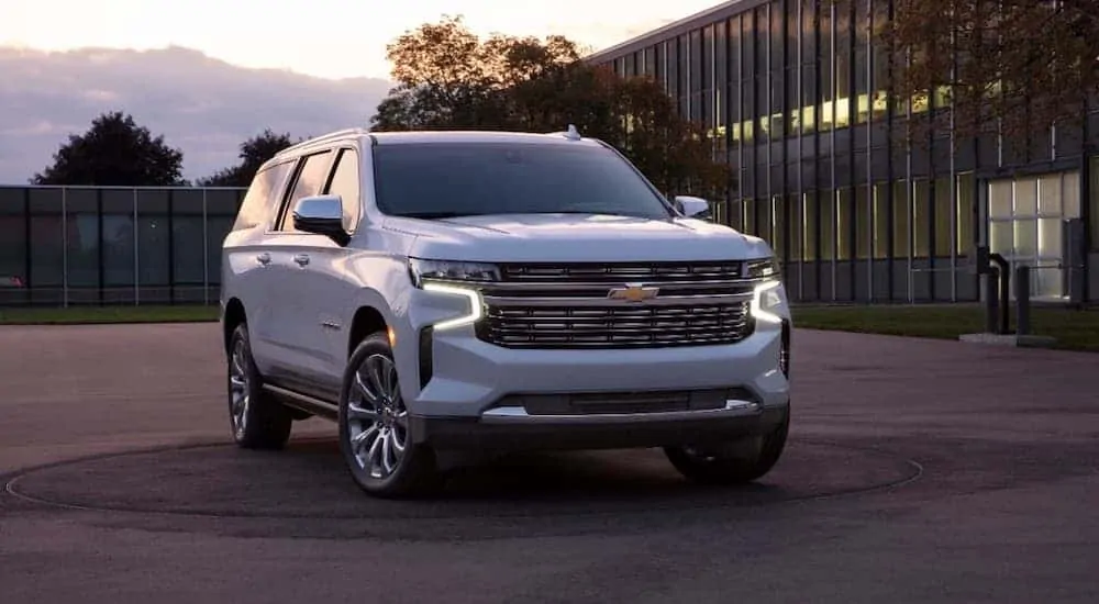 A white 2021 Chevy Suburban is parked in front of a glass building at sunset.