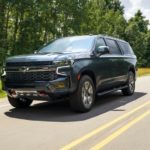 A gray 2021 Chevy Suburban Z71 is driving on a tree-lined road.