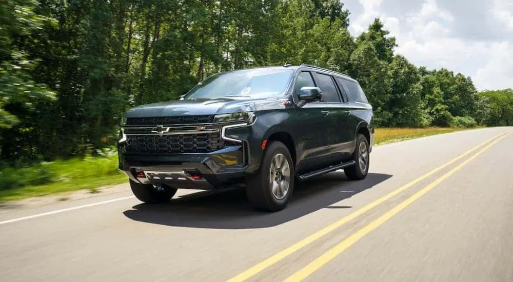 A gray 2021 Chevy Suburban Z71 is driving on a tree-lined road.