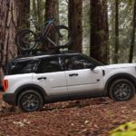 A silver 2021 Ford Bronco Sport with bikes on the roof is driving through a woodland trail.