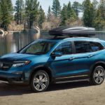 A blue 2021 Honda Pilot is parked in front of a pond with a luggage carrier on top.