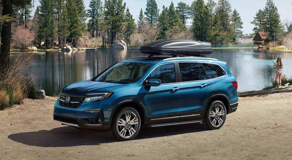 A blue 2021 Honda Pilot is parked in front of a pond with a luggage carrier on top.
