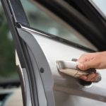 A closeup shows a hand opening the door of a silver car.