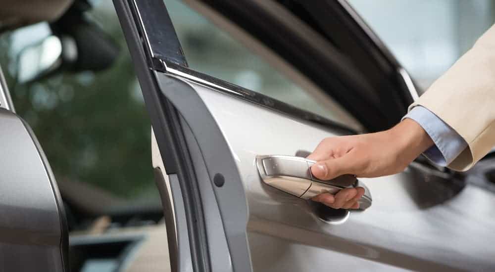 A closeup shows a hand opening the door of a silver car.