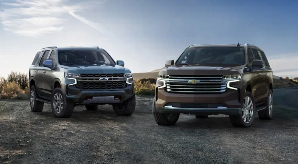 A grey 2021 Chevy Tahoe is parked next to a brown Suburban on a rural road.