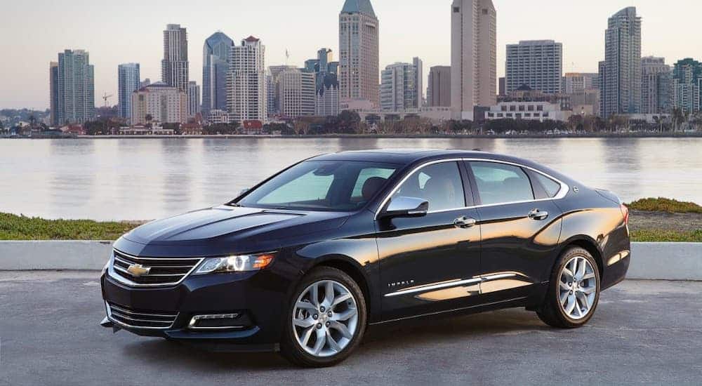 A black 2020 Chevy Impala is parked in front of a river and city.