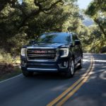 A black 2021 GMC Yukon is driving on a tree-lined road after leaving a GMC dealer.