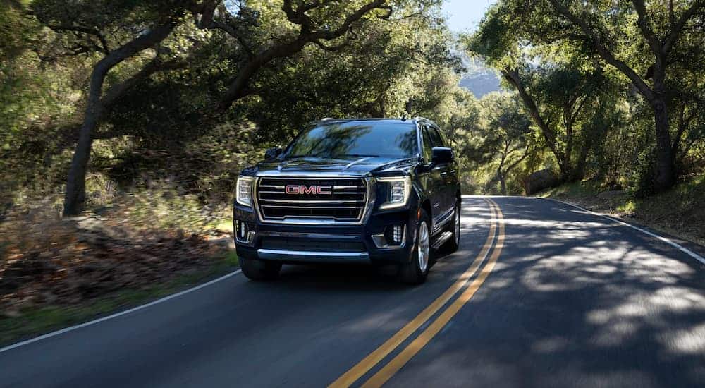 A black 2021 GMC Yukon is driving on a tree-lined road after leaving a GMC dealer.