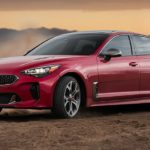 A red 2020 Kia Stinger is drifting on dirt at sunset.