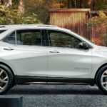 A white 2020 Chevy Equinox, which is a popular new vehicle for sale, is parked in front of a wood-sided home.