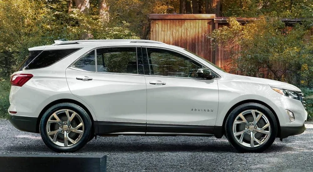 A white 2020 Chevy Equinox, which is a popular new vehicle for sale, is parked in front of a wood-sided home.