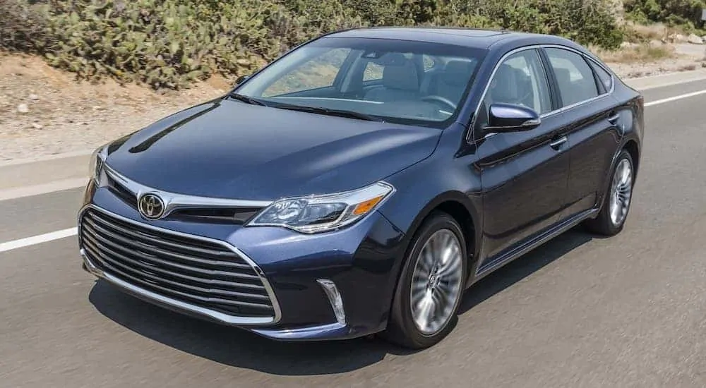 A blue 2017 Toyota Avalon from your local used car dealership is driving on a desert highway.