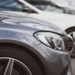 Used luxury cars from a used car dealership are parked in a row, shown from a closeup of the front fenders.