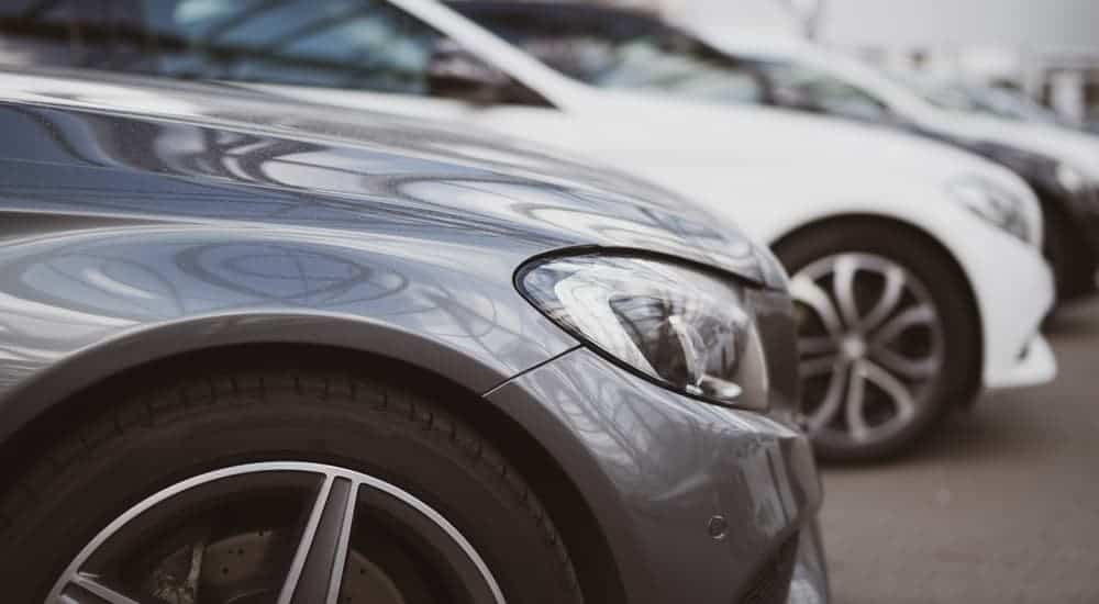 Used luxury cars from a used car dealership are parked in a row, shown from a closeup of the front fenders.