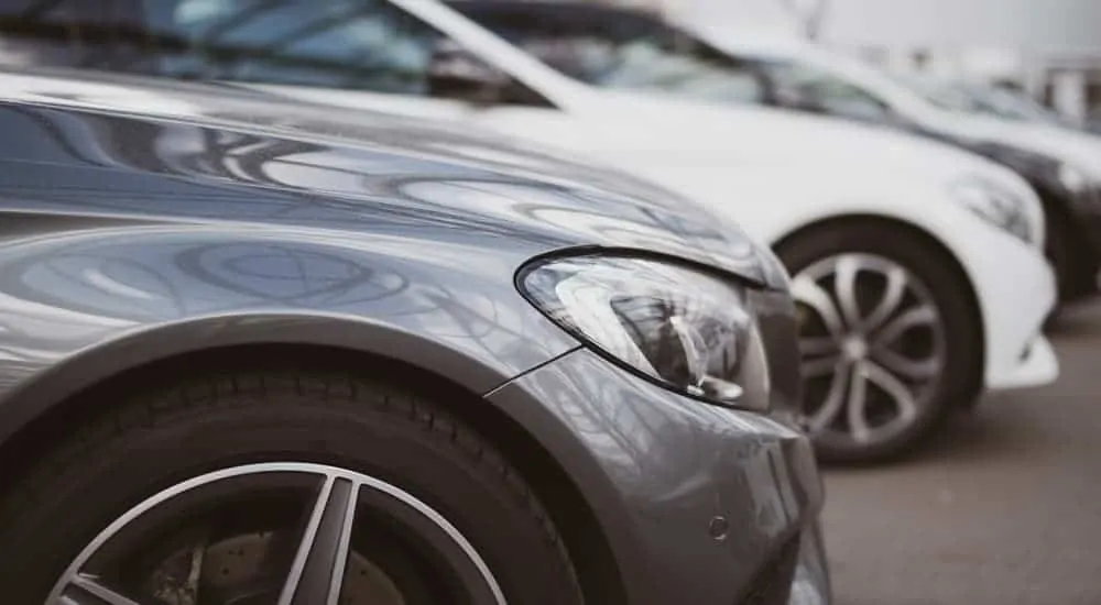 Used luxury cars from a used car dealership are parked in a row, shown from a closeup of the front fenders.