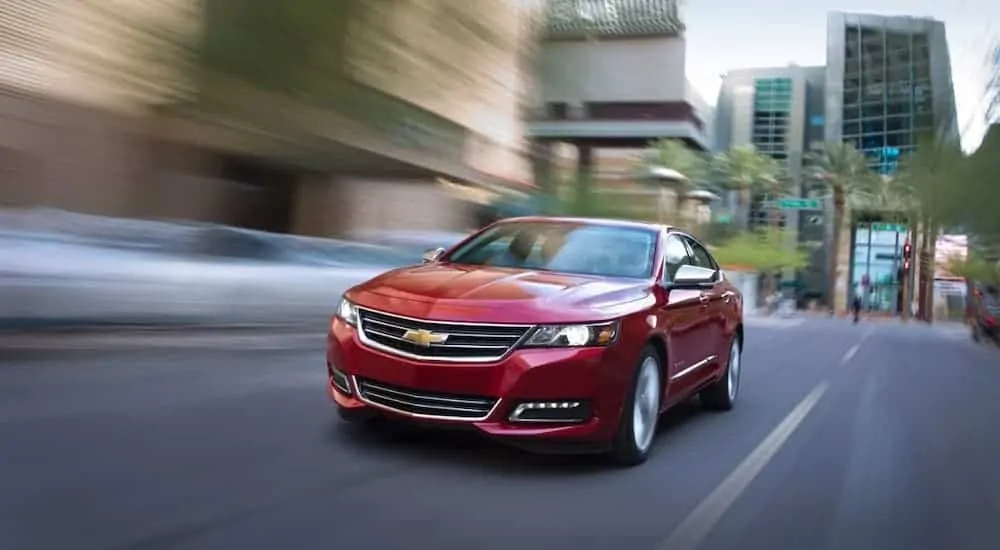 A red 2016 Chevy Impala is driving on a city street.
