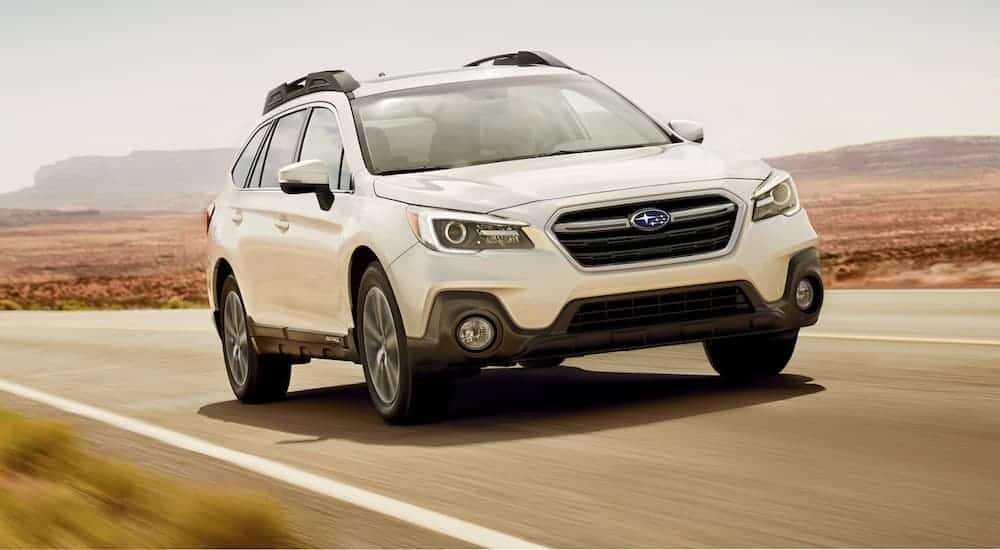 A white 2019 Subaru Outback, a popular used car, is driving on a desert road.