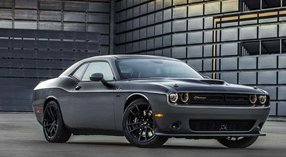 A grey 2018 Dodge Challenger, which is popular among used cars near me, is parked in front of a warehouse.