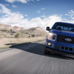 A blue 2018 Used Ford F-150 is driving past desert mountains, shown from the front.