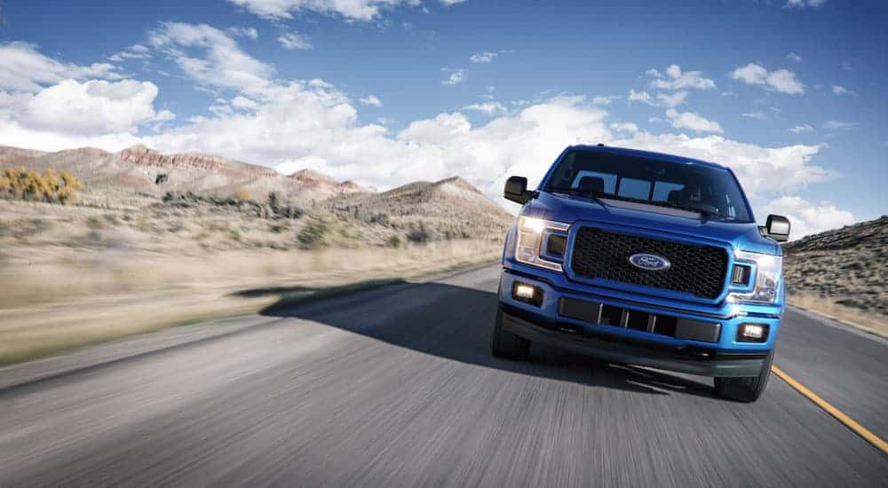 A blue 2018 Used Ford F-150 is driving past desert mountains, shown from the front.