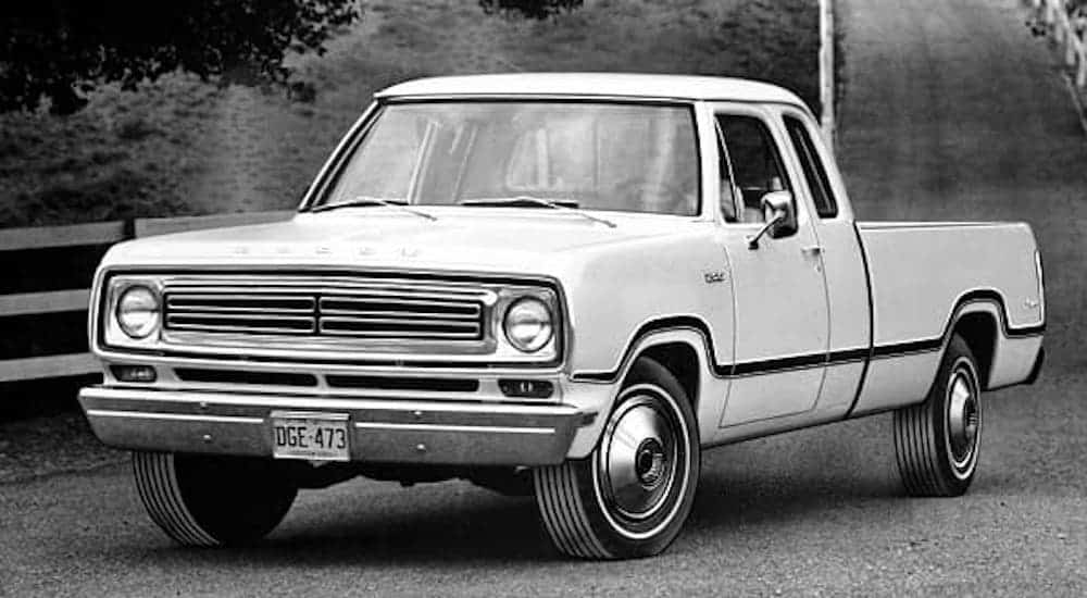 A black and white photo shows a white 1973 Ram truck on a dirt road.