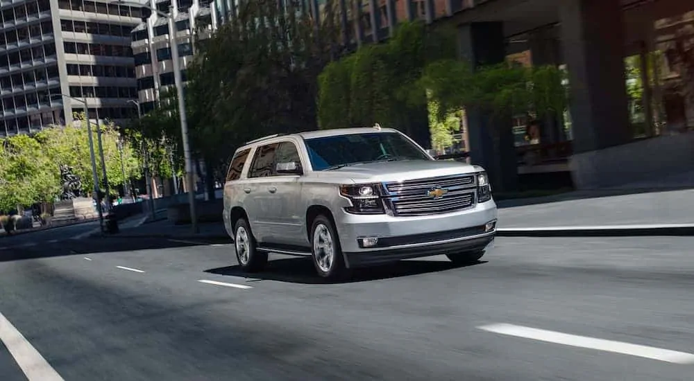 A common used Chevy Tahoe for sale, a silver 2020 Chevy Tahoe, is shown driving on a city street.