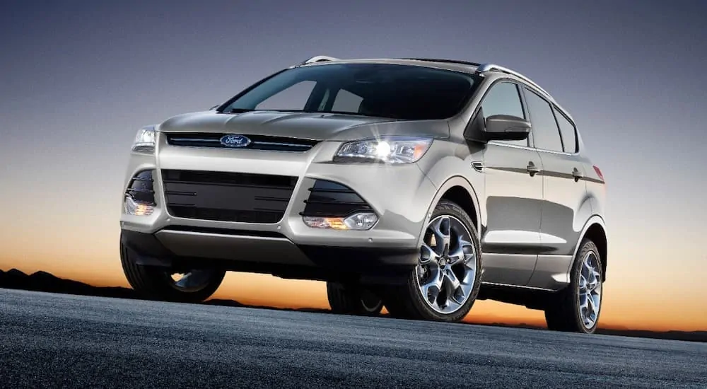 A silver 2013 used Ford Escape is parked with the sun rising behind it.