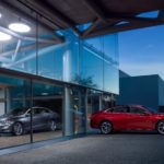 A red 2020 Chevrolet Malibu parked in front of a glass building with its mirrored image in silver on the building.