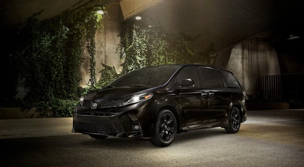 A black 2020 Toyota Sienna is parked in front of a wall covered in ivy.