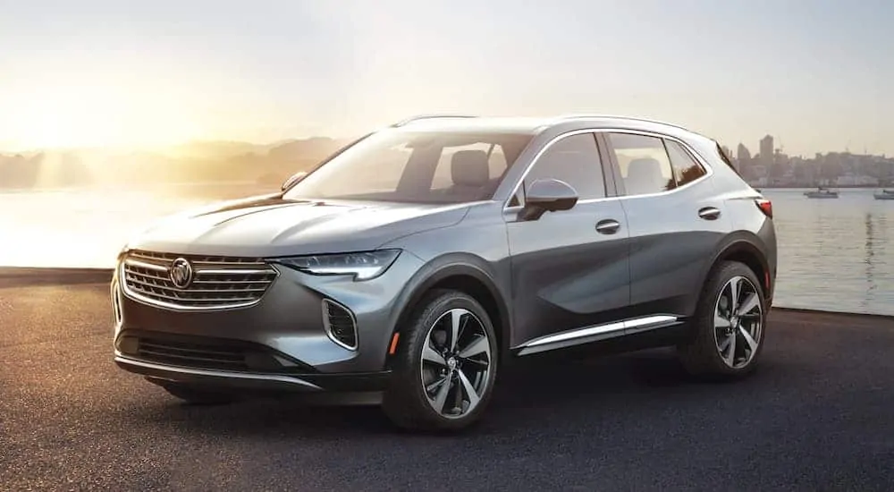 A grey 2021 Buick Envision is parked in front of a lake at sunset after a comparison of the 2021 Buick Envision vs 2020 Buick Envision.